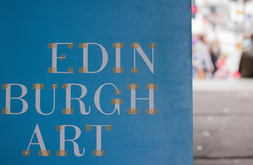 Close-up: words "Edinburgh art". This sign is on a blurred background of city street. Concept: travel to Scotland.