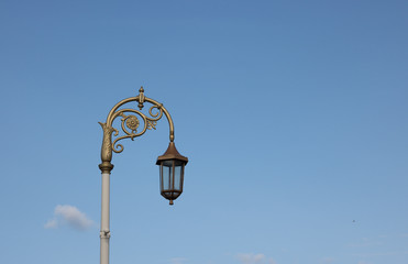 Fototapeta na wymiar Old beautiful street lamp is on a blue sky background in fine weather. One small white cloud in the sky there is only. The lantern does not light. Concept: Good morning!