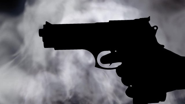 A female hand holding a pistol gun appearing and shooting. Silhouette shot over dense grey smoke.
