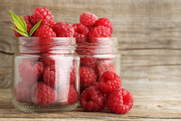 Ripe raspberries in glass jar on wooden table