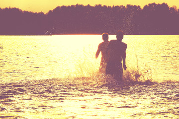 Glückliche junge Menschen laufen und springen am See beim Sonnenuntergang