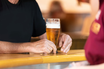 man's hand at the bar holding a glass of beer