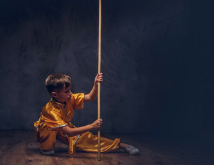 Cute boy dressed in the traditional costume of a Tibetan monk shows the tricks with dao stick from the wellness complex at a studio.