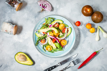 Salad with tomatoes and avocado on concrete background.