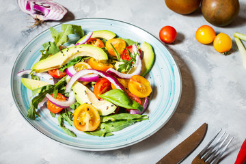 Salad with tomatoes and avocado on concrete background.