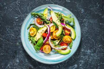 Salad with tomatoes and avocado on stone background.