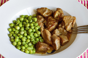 Primer plano de un plato de carnes estofada con guisantes en un plato blanco.