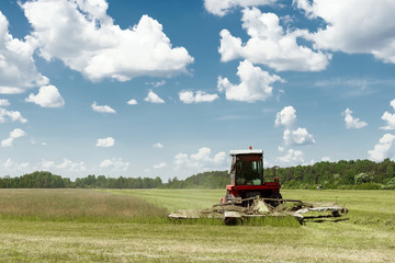 Agricultural machinery, harvester mowing grass in a field against a blue sky. Hay harvesting, grass...
