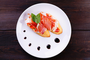 Italian bruschetta with Prosciutto di Parma and cream cheese on rustic background. Delicious snack, antipasti, appetizing toasts on white plate.