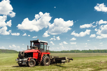 Agricultural machinery, harvester mowing grass in a field against a blue sky. Hay harvesting, grass harvesting. Season harvesting, grass, agricultural land.