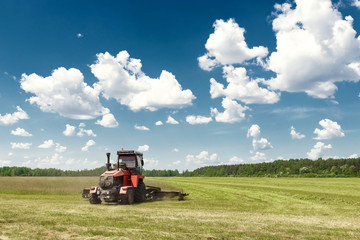 Agricultural machinery, harvester mowing grass in a field against a blue sky. Hay harvesting, grass harvesting. Season harvesting, grass, agricultural land.