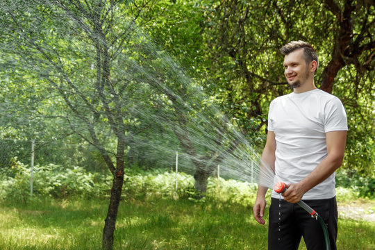 A man is watering from a hose, the concept of gardening. Hand held garden hose with water spray, watering flowers, splashing water. Copy space