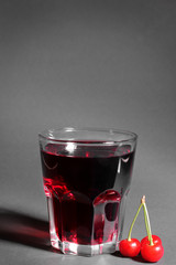 A glass of cherry juice next to a bunch of ripe, fresh cherries on a black background