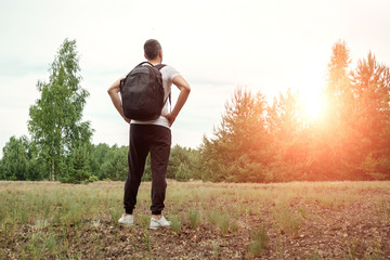 Portrait of a young man, a wanderer with a backpack. Goes on the road with a copy space, a happy tourist on a summer day, a traveler enjoying his time relaxing in nature.