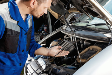 Male hands close-up, checks the oil level in the engine. The auto mechanic works in the garage. Repair service. Maintenance of the car, car repair.