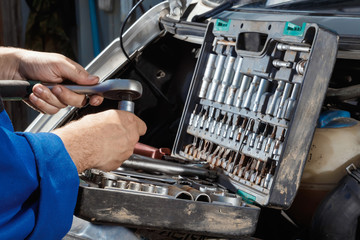 Male hands close-up with wrenches. The auto mechanic works in the garage. Repair service. Maintenance of the car, car repair.