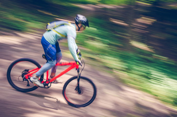 Obraz premium A cyclist in a helmet descends from the mountain on an orange bicycle, motion blur