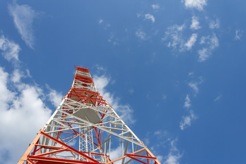 A red white telecommunications tower with a blue sky and white clouds.