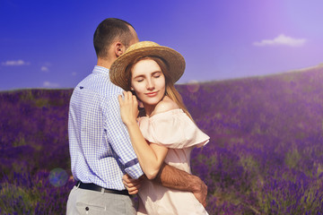 Cute young couple in love in a field of lavender flowers.  Enjoy a moment of happiness and love in a lavender field. Blond girl with hat. Romantic couple on dating. The girl hugs the guy and smile.