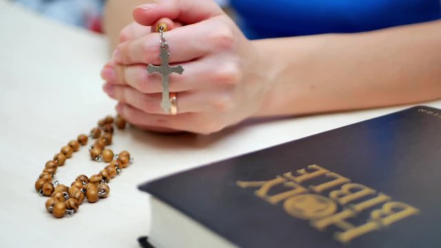 Woman prays with his fingers crossed near the Holy Bible