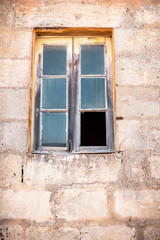 Old window with broken glass in limestone wall.