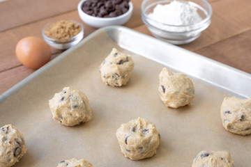 Chocolate chip cookie dough balls on parchment paper with ingredients in the background