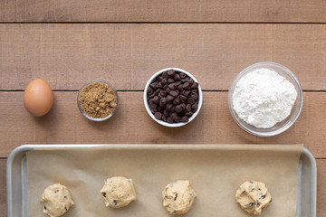 Flat lay of chocolate chip cookie ingredients, with dough balls on a baking sheet and space for text on top