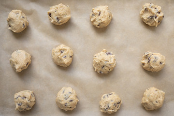 Flat lay of a grid of chocolate chip cookie dough balls on parchment paper