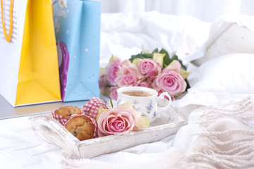 a white bed, packages with gifts, fresh coffee, breakfast cakes and a bouquet of pink roses. Good morning Vintage photo. copy space.