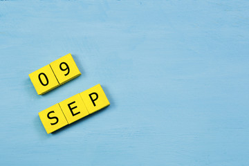 SEP 9, yellow cube calendar on blue wooden surface with copy space