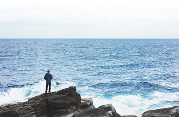 young man holds a fishing rod and catches fish in the nature on a sea background, hipster fisherman spends vacation on the blue ocean, active travel hobby fishing, rural outdoor sport tourism