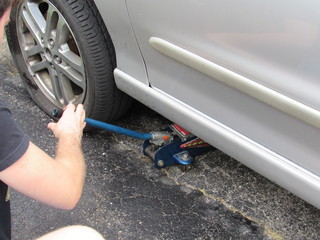 A man using a car jack to lift a car to fix a flat tire