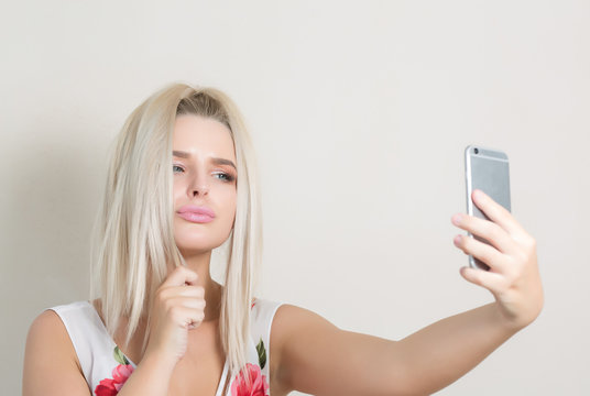 Cute blonde girl making self portrait on smartphone against a grey background