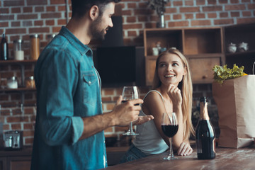 Beautiful young couple is drinking wine and smiling while cooking in kitchen at home.