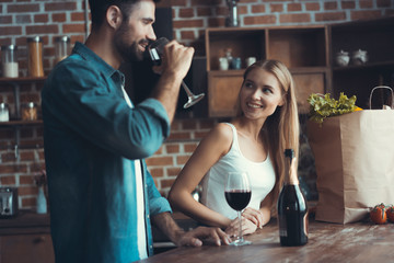 Beautiful young couple is drinking wine and smiling while cooking in kitchen at home.