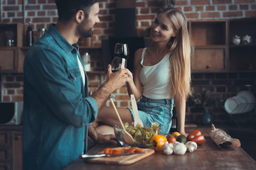 Beautiful young couple is drinking wine and smiling while cooking in kitchen at home.