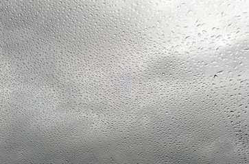 Raindrops on glass with cloud background.