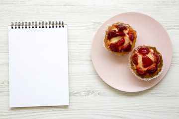Strawberry vanilla cream cheese tarts on pink plate with notebook, top view. From above, overhead.