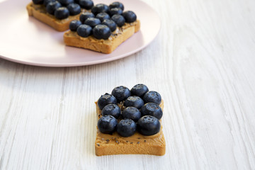 Toasts with peanut butter, blueberries and chia seeds on a white wooden table, side view. Healthy breakfast.