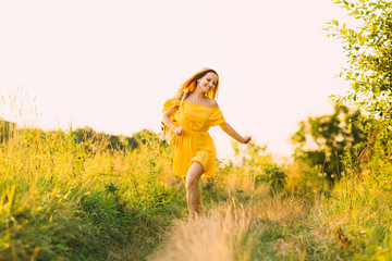 a pretty girl running in the field with high grass and cute smiles. girl in a yellow dress and a backpack on her shoulder