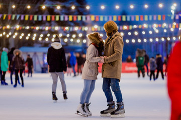 Ice skating rink and lovers together. A pair of young people in an embrace on a city skating rink lit by light bulbs and bright lights. Winter date for Christmas on the ice arena