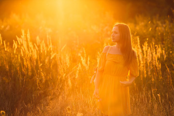 stylish girl with cute face looking into the distance on background of high grass and sunset