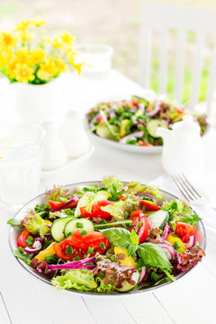 Fresh vegetarian vegetable salad with tomato, onion, cucumber, pepper, basil and lettuce. Salad on plate on white table