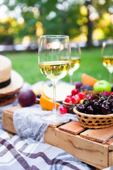 Picnic background with white wine and summer fruits on green grass, summertime party