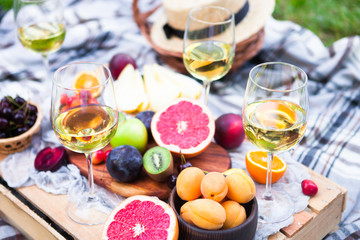 Picnic background with white wine and summer fruits on green grass, summertime party