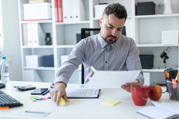 A young man in the office sits at a table, takes a marker in his hand and works with documents.