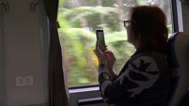 A woman is taking pictures on a smartphone from the train window