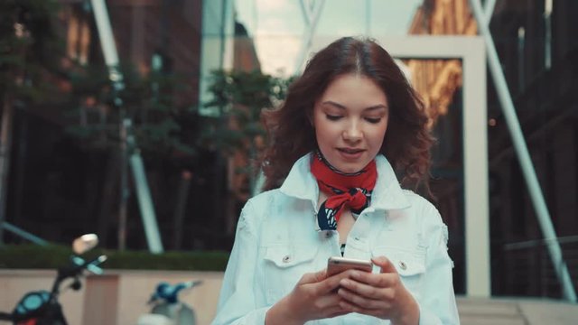 Attractive young woman with trendy hairstyle walks down the city center, checks her phone. Walking, shopping, active user, browsing the internet, texting. Female portrait