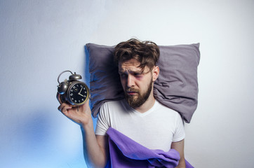 Man laying sad and awake in bed, while looking to alarm clock, sleep disorder. Copy space above head - obrazy, fototapety, plakaty