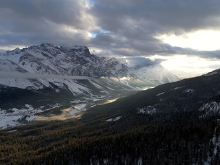 Fototapeta premium drone flying above pine tree forest on cold winter morning with sunset and alps mountain range in background